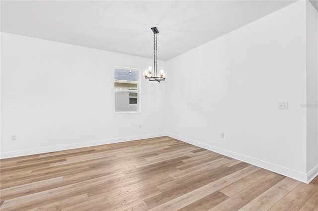 empty room featuring a chandelier, light wood-type flooring, and baseboards