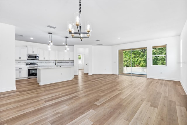 unfurnished living room featuring a sink, a chandelier, plenty of natural light, light wood-type flooring, and recessed lighting