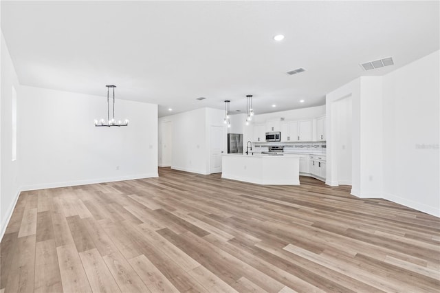 unfurnished living room with a chandelier, light wood finished floors, recessed lighting, a sink, and baseboards
