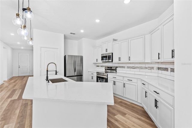 kitchen with appliances with stainless steel finishes, a sink, backsplash, recessed lighting, and a center island with sink