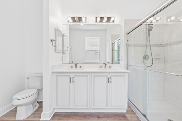 bathroom featuring toilet, a stall shower, double vanity, and wood finished floors