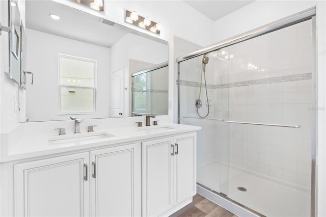 bathroom with a stall shower, double vanity, and wood finished floors