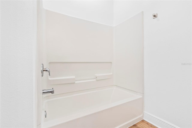 full bath with baseboards, wood finished floors, and washtub / shower combination