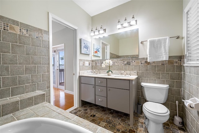 401 Whitcomb Blvd, Tarpon Springs, FL 34689 - bathroom featuring tile walls, toilet, double vanity, and a wainscoted wall