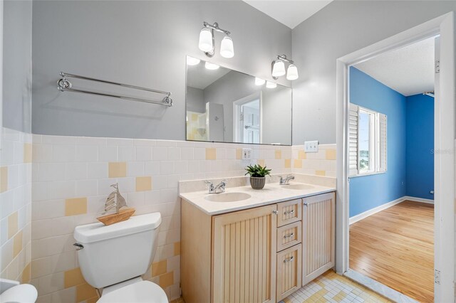 401 Whitcomb Blvd, Tarpon Springs, FL 34689 - bathroom featuring toilet, double vanity, tile patterned flooring, tile walls, and a wainscoted wall
