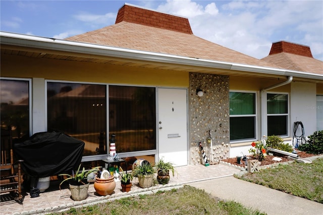 view of exterior entry featuring a chimney, roof with shingles, and stucco siding