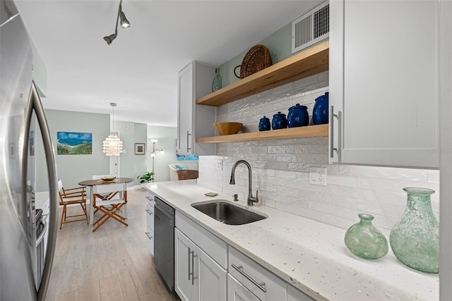 kitchen with freestanding refrigerator, a sink, dishwasher, decorative backsplash, and light wood-style floors