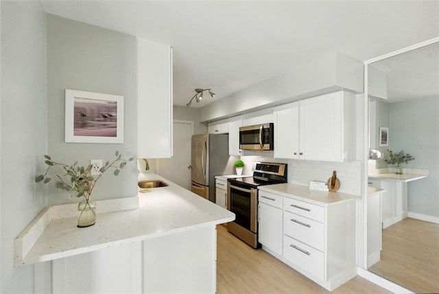 kitchen featuring appliances with stainless steel finishes, light wood finished floors, a sink, decorative backsplash, and white cabinetry