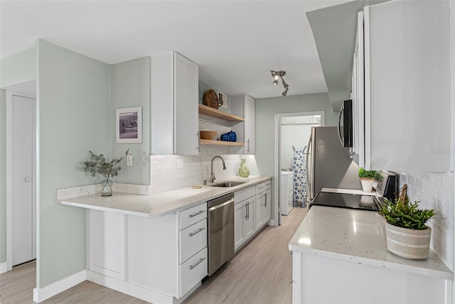kitchen with stainless steel dishwasher, a sink, backsplash, range, and light wood finished floors