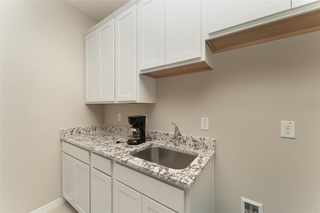 kitchen featuring a sink, white cabinets, light stone counters, and baseboards