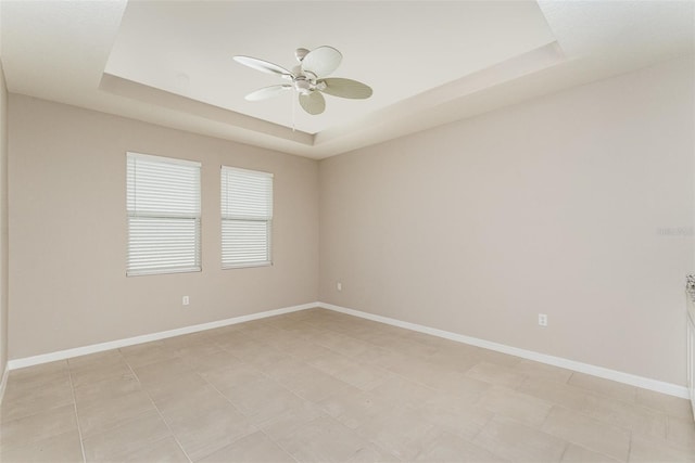 unfurnished room with a raised ceiling, ceiling fan, and baseboards