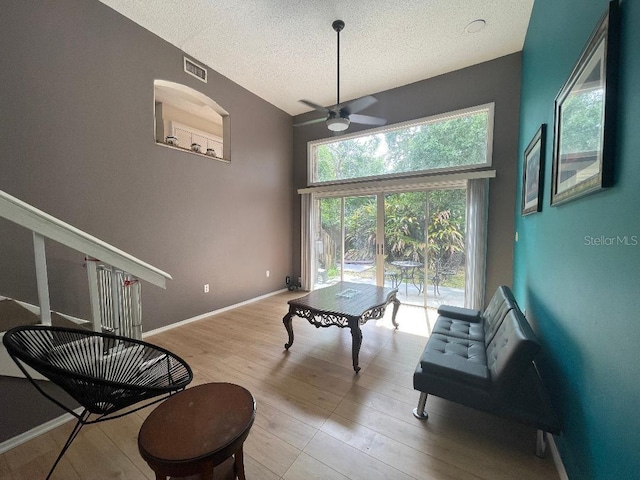 living area with a ceiling fan, a textured ceiling, wood finished floors, baseboards, and a towering ceiling