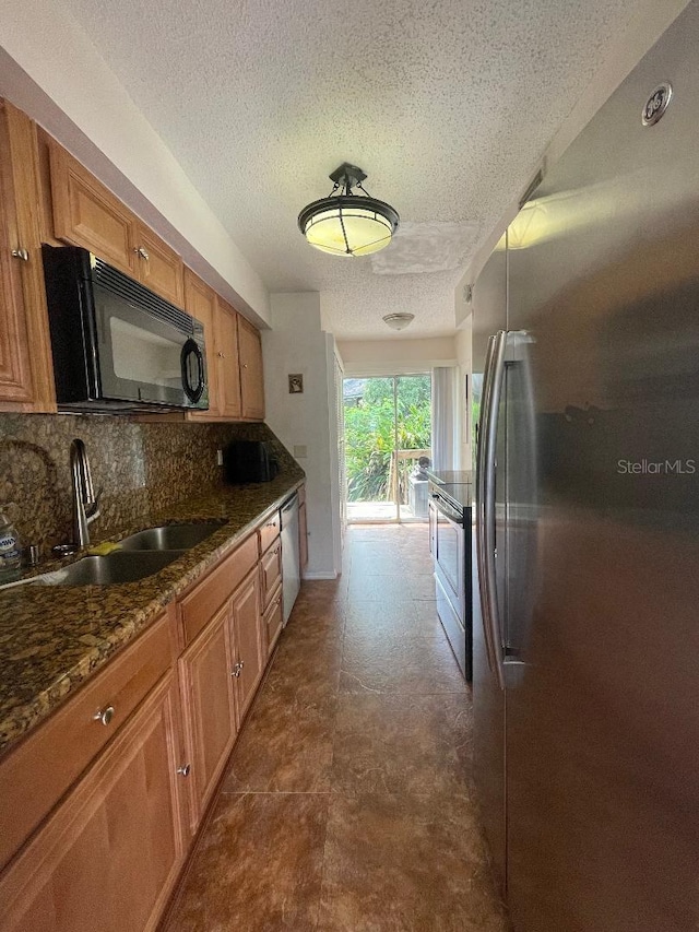 kitchen with stainless steel appliances, a sink, a textured ceiling, brown cabinetry, and tasteful backsplash