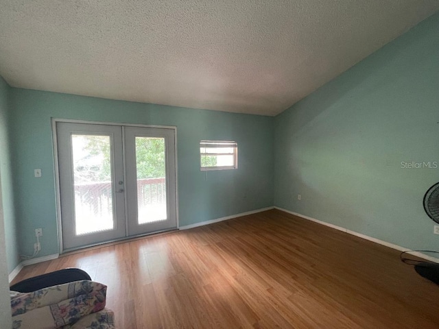 empty room featuring french doors, wood finished floors, a textured ceiling, and baseboards