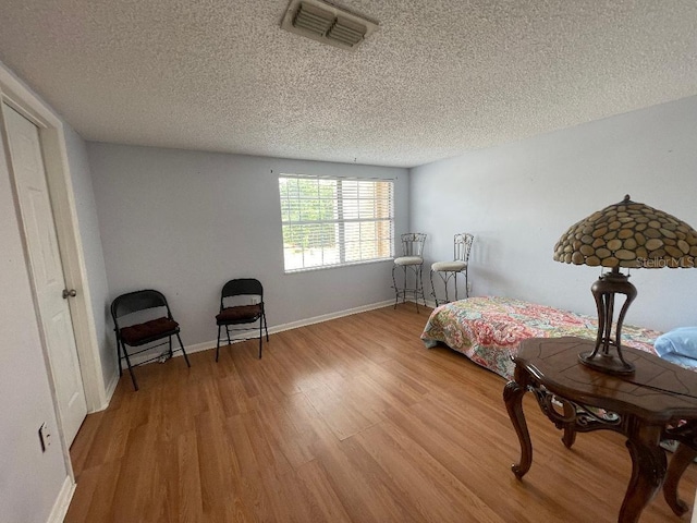 bedroom featuring a textured ceiling, light wood-style flooring, and baseboards