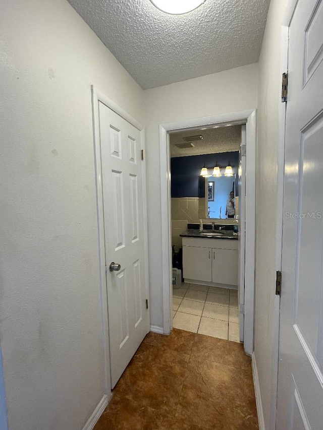 corridor featuring a textured ceiling, light tile patterned floors, a sink, and baseboards