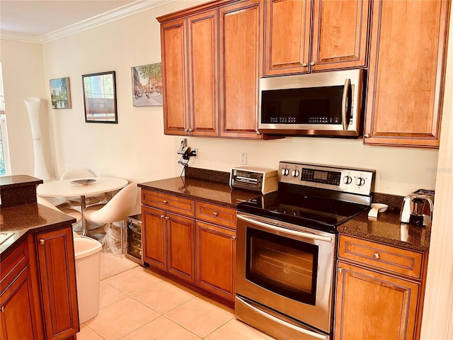 184 Banyan Bay Dr, Saint Petersburg, FL 33705 - kitchen featuring stainless steel appliances, light tile patterned flooring, dark stone countertops, crown molding, and brown cabinetry