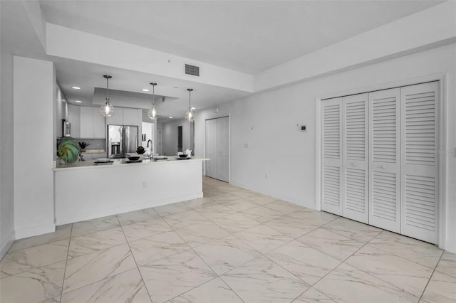 kitchen featuring stainless steel refrigerator with ice dispenser, light marble finish floors, a peninsula, recessed lighting, and pendant lighting