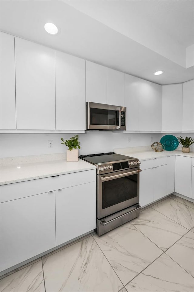 kitchen with appliances with stainless steel finishes, light marble finish floors, white cabinets, light countertops, and recessed lighting