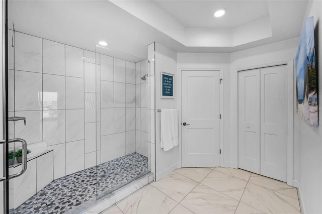 bathroom with a tile shower, a raised ceiling, recessed lighting, marble finish flooring, and baseboards