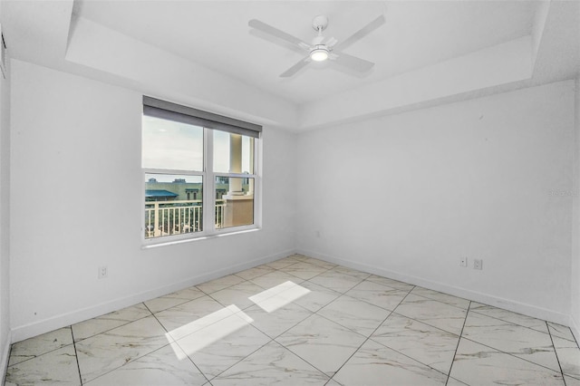 unfurnished room with a raised ceiling, baseboards, a ceiling fan, and light marble finish floors