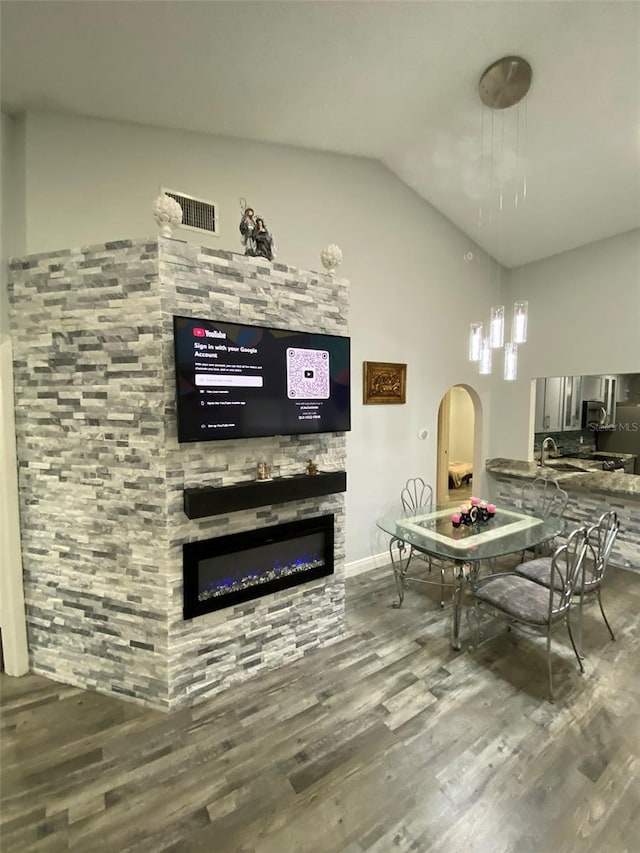 2390 Bentley Dr, Palm Harbor, FL 34684 - living area featuring wood finished floors, vaulted ceiling, a glass covered fireplace, and arched walkways