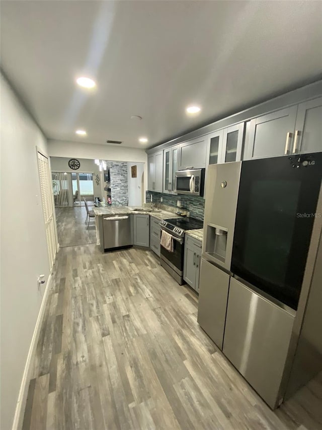 2390 Bentley Dr, Palm Harbor, FL 34684 - kitchen with stainless steel appliances, a peninsula, tasteful backsplash, glass insert cabinets, and light wood finished floors