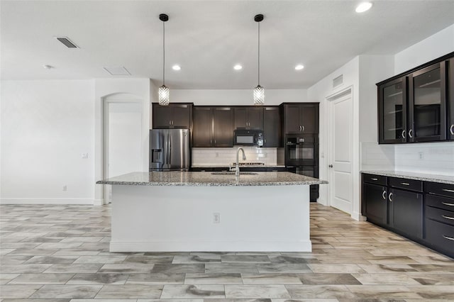 12710 Wheatgrass Ct, Parrish, FL 34219 - kitchen with black appliances, decorative backsplash, light stone countertops, a sink, and a center island with sink
