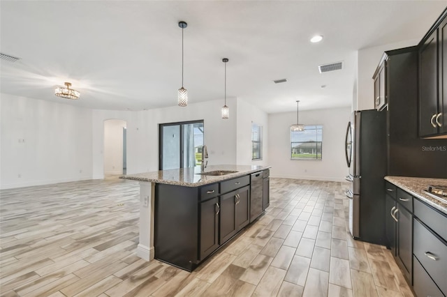 12710 Wheatgrass Ct, Parrish, FL 34219 - kitchen with a sink, arched walkways, a center island with sink, open floor plan, and light wood-style flooring