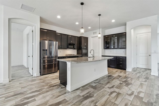 12710 Wheatgrass Ct, Parrish, FL 34219 - kitchen featuring black appliances, a sink, tasteful backsplash, light wood-style floors, and a kitchen island with sink