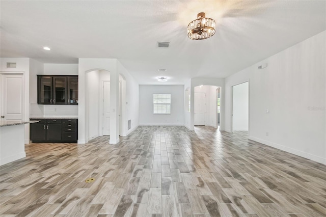 12710 Wheatgrass Ct, Parrish, FL 34219 - unfurnished living room with arched walkways, light wood finished floors, baseboards, recessed lighting, and a chandelier