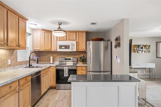 kitchen featuring stainless steel appliances, a sink, decorative backsplash, light wood-style flooring, and a kitchen island