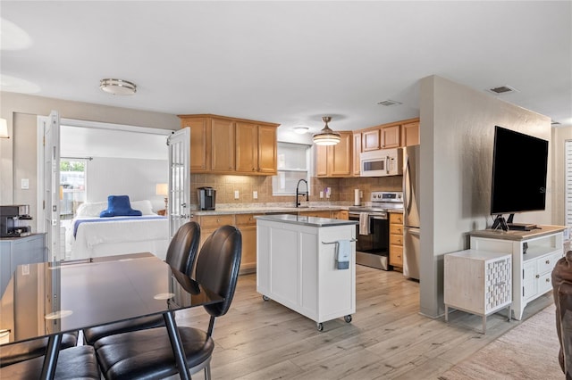 kitchen with appliances with stainless steel finishes, light wood-type flooring, decorative backsplash, light countertops, and a kitchen island