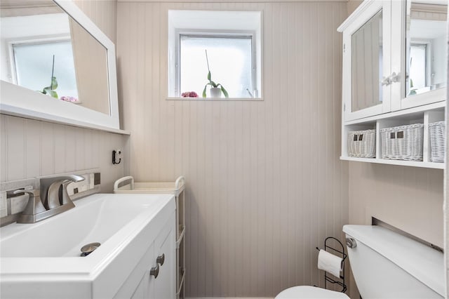 half bathroom featuring toilet, vanity, and wood walls