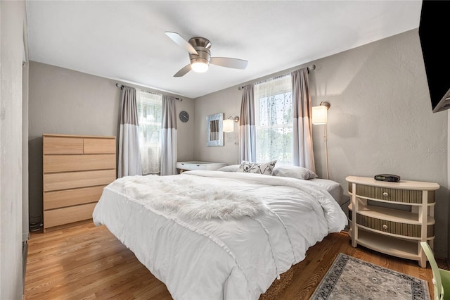 bedroom featuring wood finished floors, a textured wall, and ceiling fan