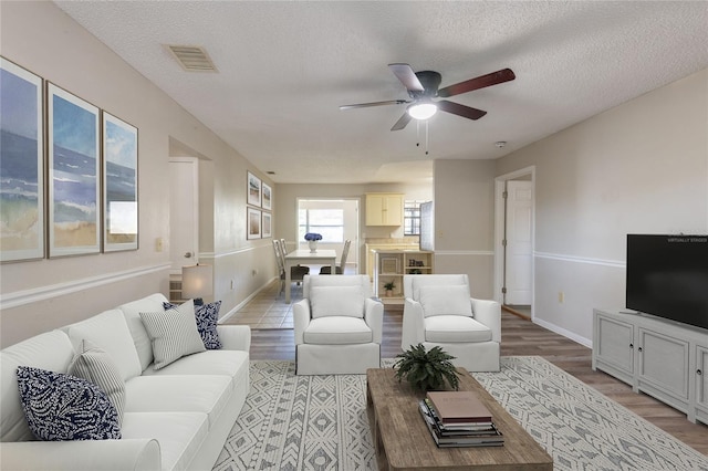 living area featuring light wood-style flooring, a ceiling fan, a textured ceiling, and baseboards