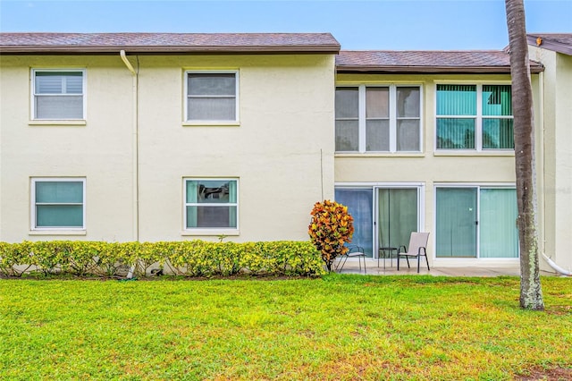 1100 E Bay Dr Unit 60, Largo, FL 33770 - rear view of house featuring stucco siding, a lawn, roof with shingles, and a patio