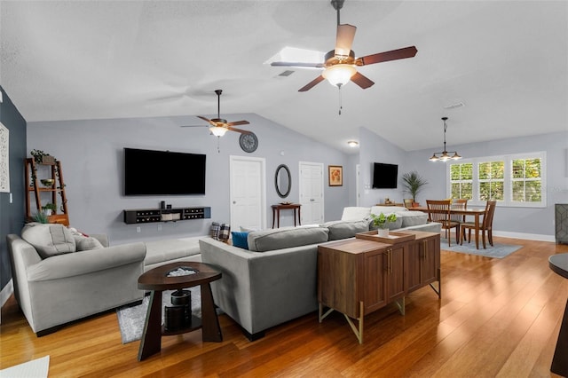 living area featuring light wood finished floors, a ceiling fan, vaulted ceiling, a chandelier, and baseboards