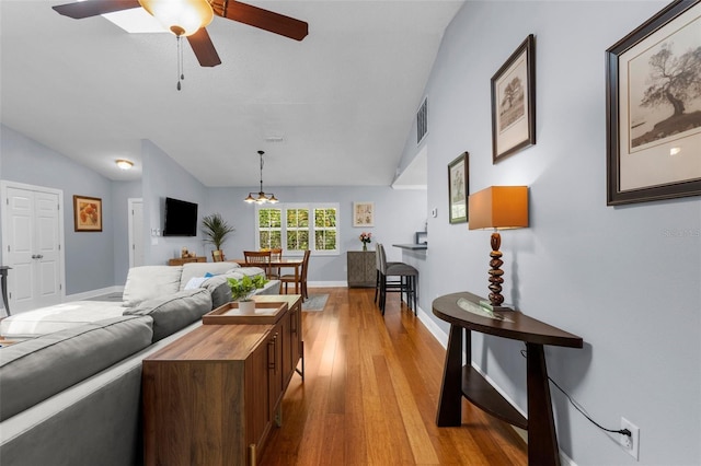 living room featuring vaulted ceiling, light wood-style flooring, a ceiling fan, baseboards, and a chandelier