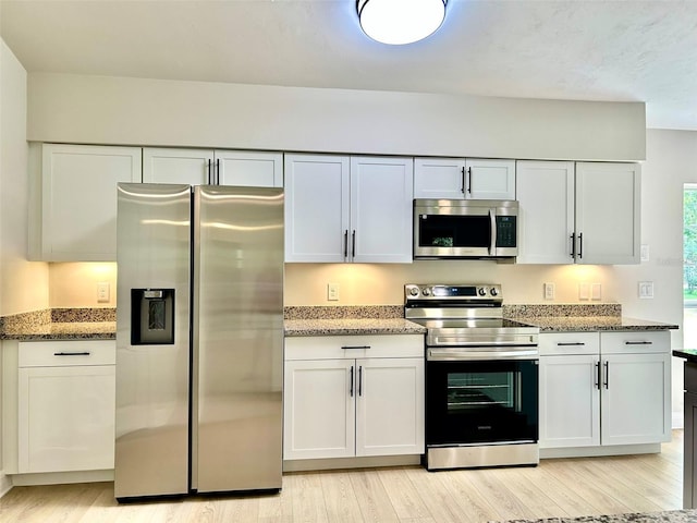 607 NE 10th Blvd, Williston, FL 32696 - kitchen featuring appliances with stainless steel finishes, light wood-type flooring, light stone counters, and white cabinets