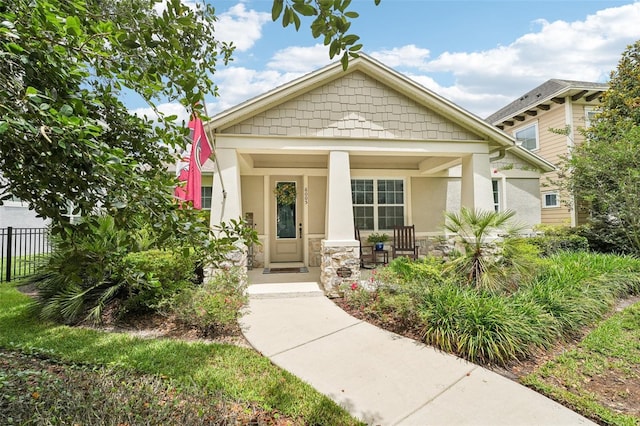 craftsman-style house with covered porch, stucco siding, fence, and stone siding