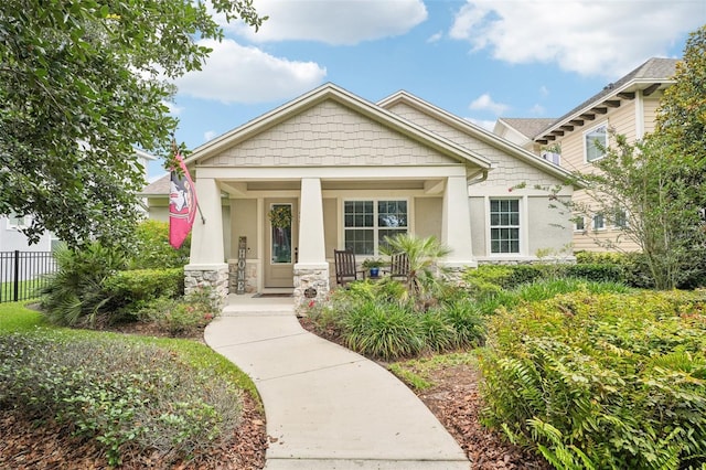 craftsman-style home featuring stucco siding, covered porch, fence, and stone siding
