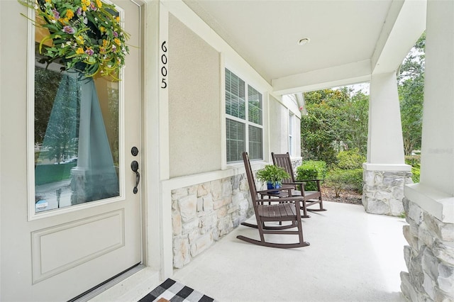 property entrance featuring covered porch, stone siding, and stucco siding