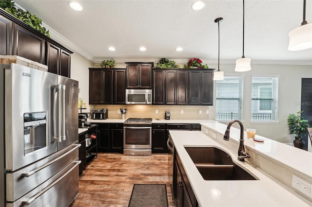 kitchen featuring stainless steel appliances, a sink, crown molding, light countertops, and light wood finished floors