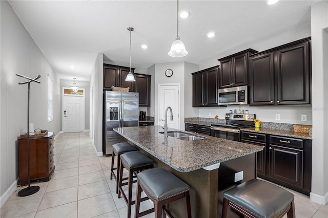 kitchen featuring a sink, stainless steel appliances, a breakfast bar area, dark stone counters, and baseboards
