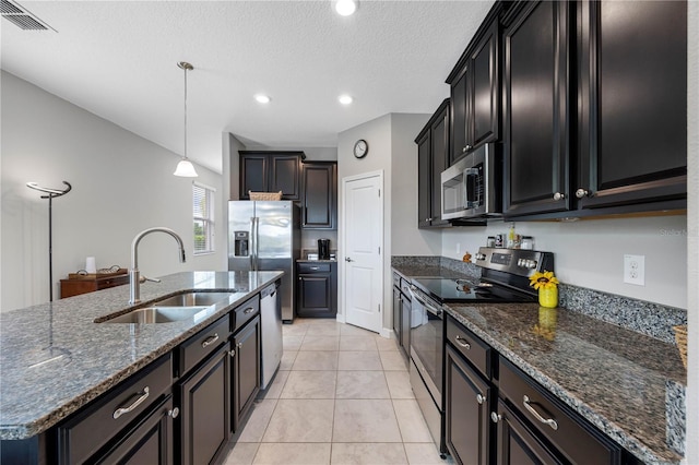 kitchen with stainless steel appliances, a sink, pendant lighting, dark stone counters, and an island with sink