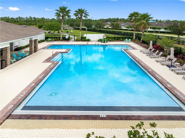 community pool featuring a patio area, view of scattered trees, and fence