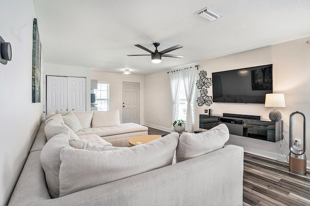 living area featuring dark wood finished floors, a ceiling fan, a textured ceiling, and baseboards