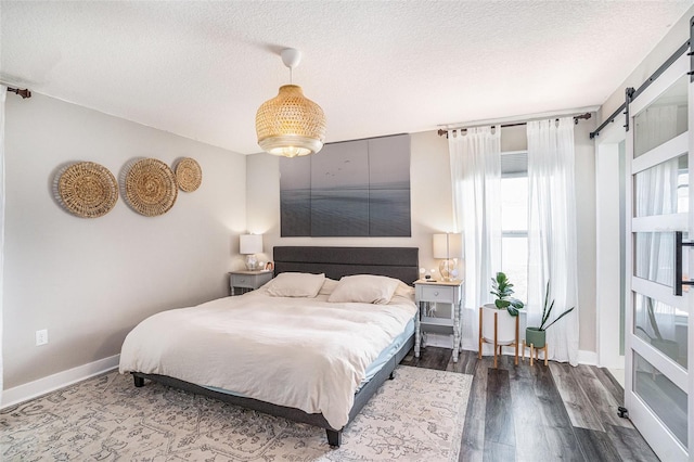 bedroom with a barn door, a textured ceiling, dark wood finished floors, and baseboards