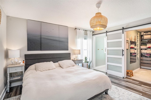 bedroom featuring wood finished floors, a barn door, baseboards, a textured ceiling, and a spacious closet